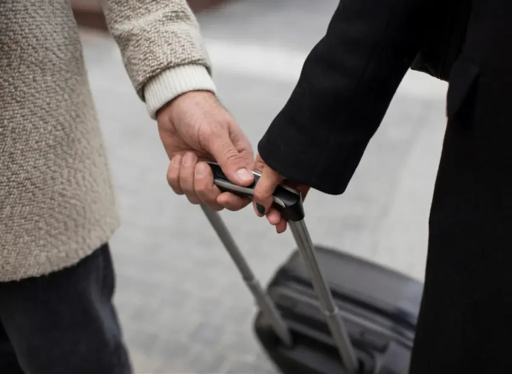 Una pareja tomada de la mano mientras viajan juntos, empujando una maleta por la calle, indicando un viaje o reubicación.